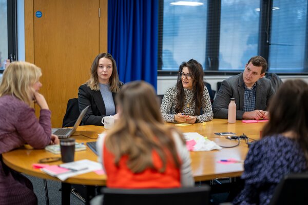 Shayda Kashef sitting at a round table with five other people at a meeting to discuss public engagement. 